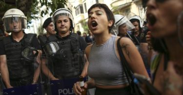 Teilnehmende der Pride-Parade in Istanbul stehen neben Polizisten und rufen Slogans. Foto: Emrah Gurel/AP/dpa