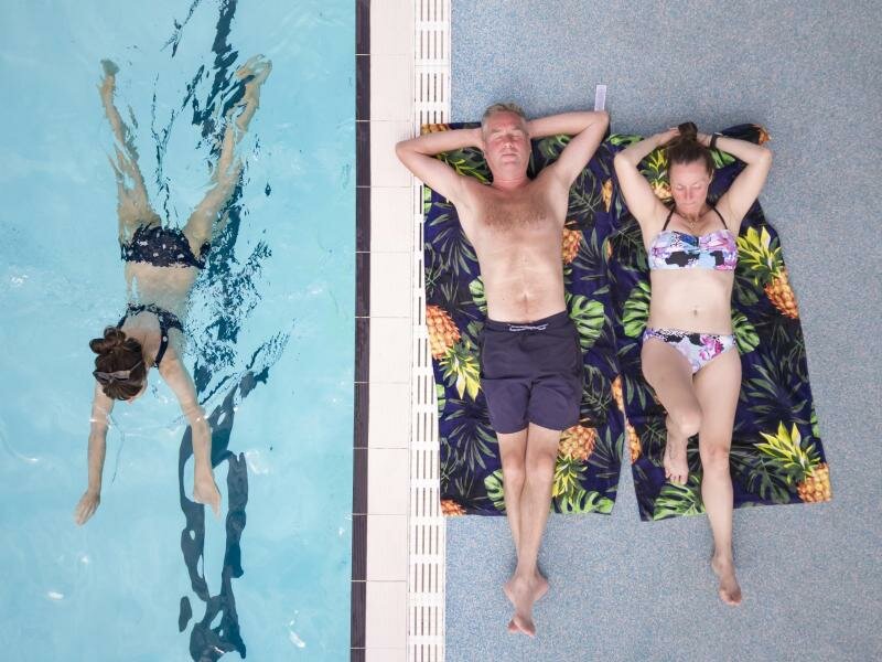 Ein Paar liegt auf Badetüchern neben einem Schwimmbecken im britischen Hathersage. Foto: Danny Lawson/PA Wire/dpa
