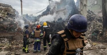 Ukrainische Feuerwehrleute stehen vor einer zerstörten Schule nach einem Beschuss. Foto: Alex Chan Tsz Yuk/SOPA Images via ZUMA Press Wire/dpa