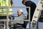 Papst Franziskus (l.) wird in einem Rollstuhl in ein Flugzeug am Internationalen Flughafen Leonardo da Vinci geschoben. Foto: Riccardo De Luca/AP/dpa