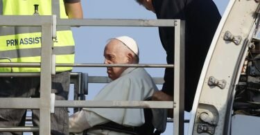 Papst Franziskus (l.) wird in einem Rollstuhl in ein Flugzeug am Internationalen Flughafen Leonardo da Vinci geschoben. Foto: Riccardo De Luca/AP/dpa