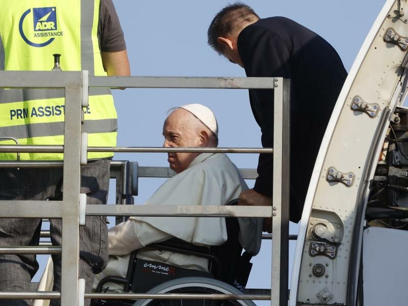 Papst Franziskus (l.) wird in einem Rollstuhl in ein Flugzeug am Internationalen Flughafen Leonardo da Vinci geschoben. Foto: Riccardo De Luca/AP/dpa