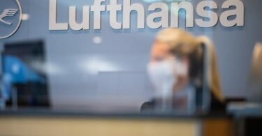 Eine Mitarbeiterin der Lufthansa sitzt mit ihrer Mund- und Nasenschutzmaske am Check-in im Flughafen Münster-Osnabrück. Foto: Guido Kirchner/dpa
