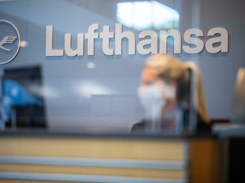 Eine Mitarbeiterin der Lufthansa sitzt mit ihrer Mund- und Nasenschutzmaske am Check-in im Flughafen Münster-Osnabrück. Foto: Guido Kirchner/dpa