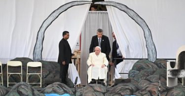 Papst Franziskus wird in seinem Rollstuhl auf die Bühne geschoben. Foto: Johannes Neudecker/dpa