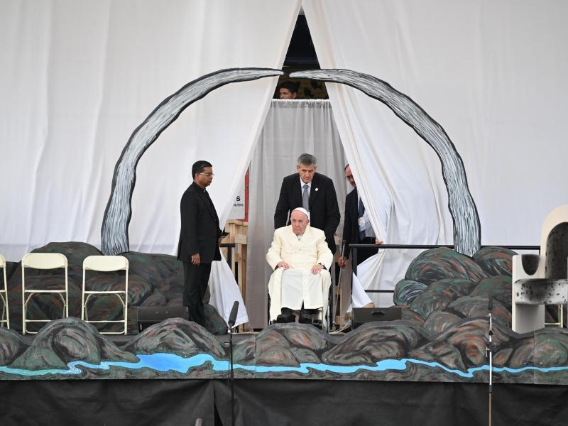 Papst Franziskus wird in seinem Rollstuhl auf die Bühne geschoben. Foto: Johannes Neudecker/dpa