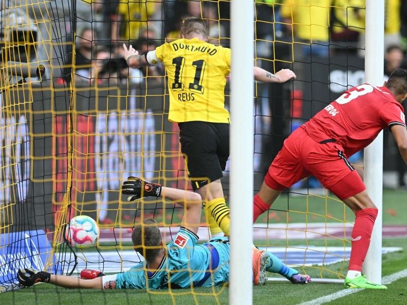 Dortmunds Marco Reus (M) stochert den Ball gegen Leverkusens Torwart Lukas Hradecky (l) und Piero Hincapie über die Linie. Foto: Bernd Thissen/dpa