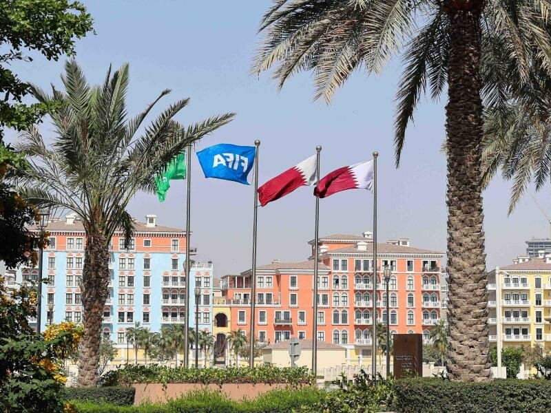 Flaggen in den Farben Katars und eine Fifa-Flagge wehen unter Palmen. Foto: Christian Charisius/dpa