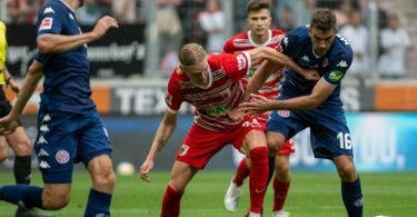 Augsburgs Fredrik Jensen (l) und Mainz Stefan Bell kämpfen körperbetont um den Ball. Foto: Stefan Puchner/dpa