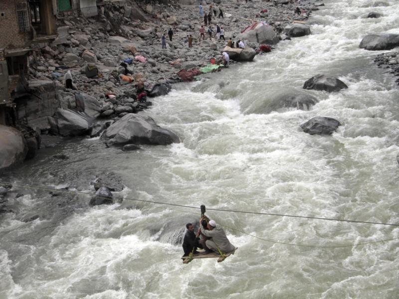 Menschen überqueren einen Fluss mithilfe einer Seilbahn. Foto: Naveed Ali/AP/dpa
