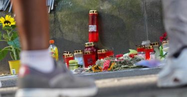 Menschen stehen in Dortmund vor einem Zaun, an dem mit Kerzen und Blumen des von der Polizei erschossenen Jugendlichen gedacht wird. Foto: Gregor Bauernfeind/dpa