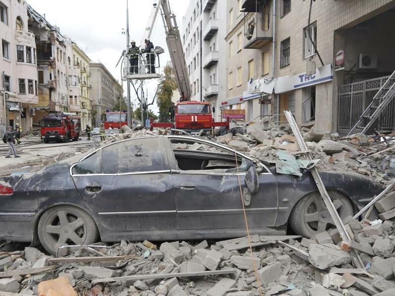 Feuerwehrleute stehen nach einem Raketenangriff des russischen Militärs auf einem Kran auf einer Straße in Charkiw. Foto: Andrii Marienko/AP/dpa
