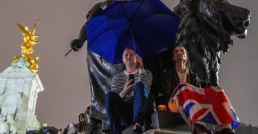 Menschen versammeln sich mit Regenschirmen und Flaggen, um Königin Elizabeth II. die letzte Ehre zu erweisen. Foto: Jasmine Leung/SOPA Images via ZUMA Press Wire/dpa