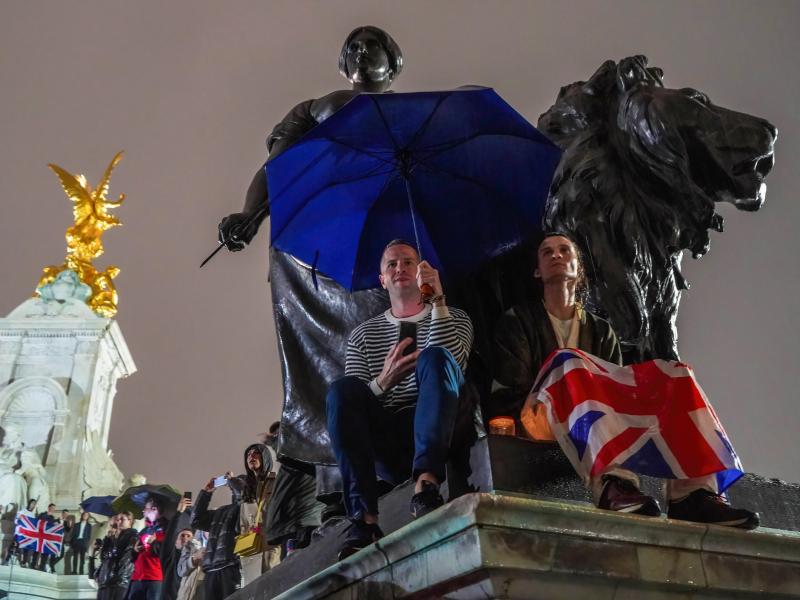 Menschen versammeln sich mit Regenschirmen und Flaggen, um Königin Elizabeth II. die letzte Ehre zu erweisen. Foto: Jasmine Leung/SOPA Images via ZUMA Press Wire/dpa