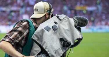 Ein Kameramann steht am Spielfeldrand und filmt ein Fußballspiel. Foto: Tom Weller/dpa