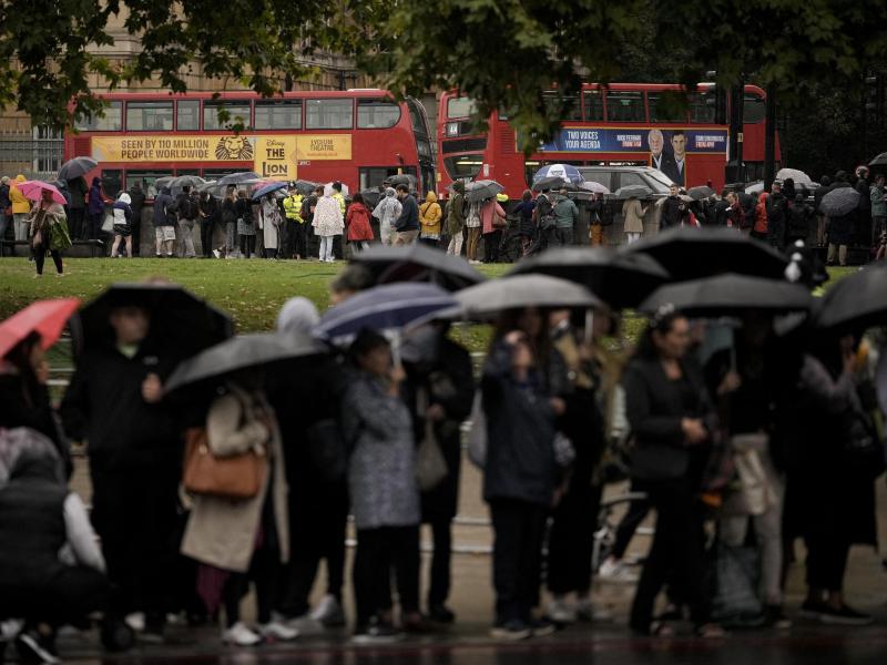 Menschen stehen auf der Straße und warten auf den Leichenwagen mit dem Sarg von Königin Elizabeth II. Foto: Andreea Alexandru/AP/dpa