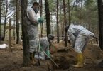 Arbeiter stehen auf dem Waldfriedhof von Isjum am Grab eines nicht identifizierten Zivilisten. Dort wurden nach Angaben aus Kiew mehr als 400 Leichen gefunden. Die Menschen sollen ums Leben gekommen sein, als Russland die Stadt Ende März beschoss. Foto: Evgeniy Maloletka/AP/dpa