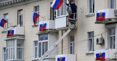 Arbeiter hängen russische Fahnen an einem Wohnhaus in der von Russland unterstützten und von Separatisten kontrollierten Volksrepublik Luhansk auf. Foto: Uncredited/AP/dpa