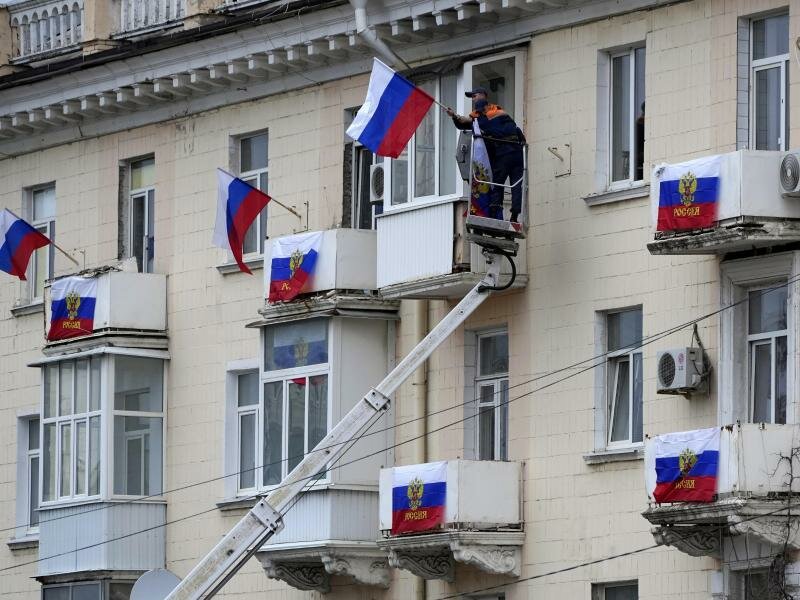 Arbeiter hängen russische Fahnen an einem Wohnhaus in der von Russland unterstützten und von Separatisten kontrollierten Volksrepublik Luhansk auf. Foto: Uncredited/AP/dpa